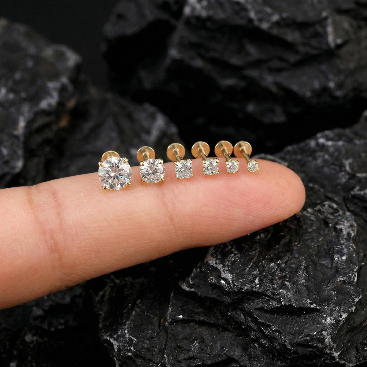 A close-up image of a person's finger wearing a row of gold-colored diamond stud earrings.