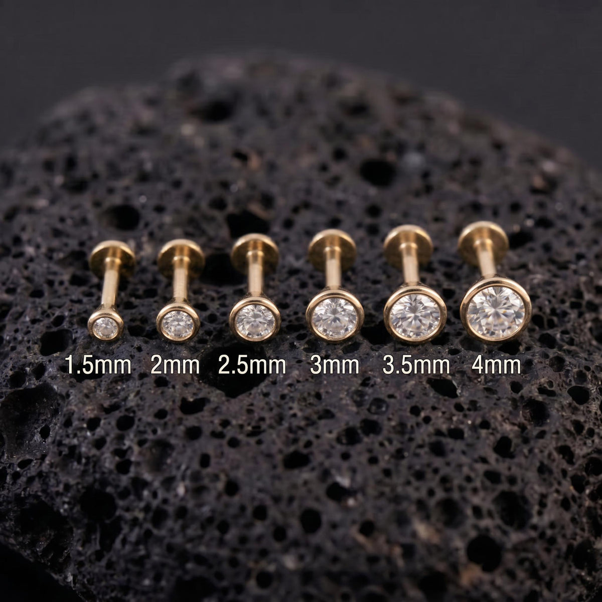 A collection of gold-colored diamond stud earrings with varying sizes, ranging from 1.5mm to 4mm, displayed on a dark surface.