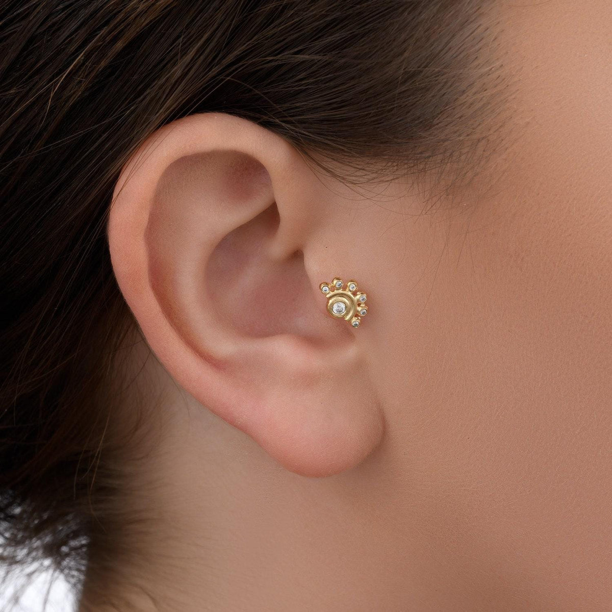 A close-up view of a person's ear with a gold earring featuring a floral design.