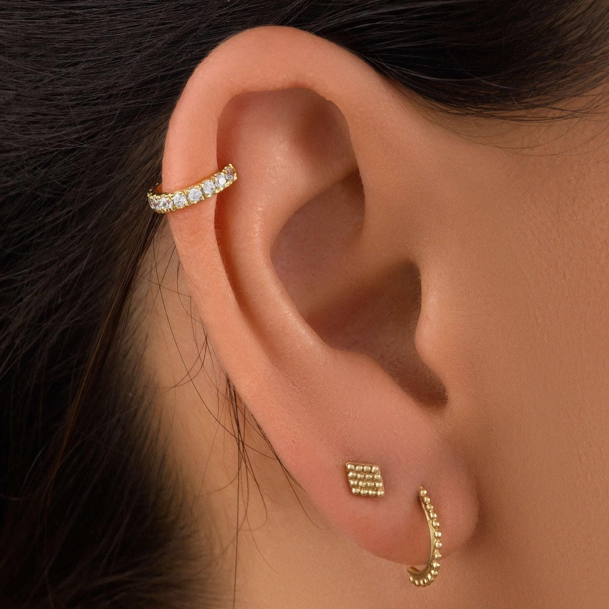 A close-up view of a person's ear adorned with three gold earrings.