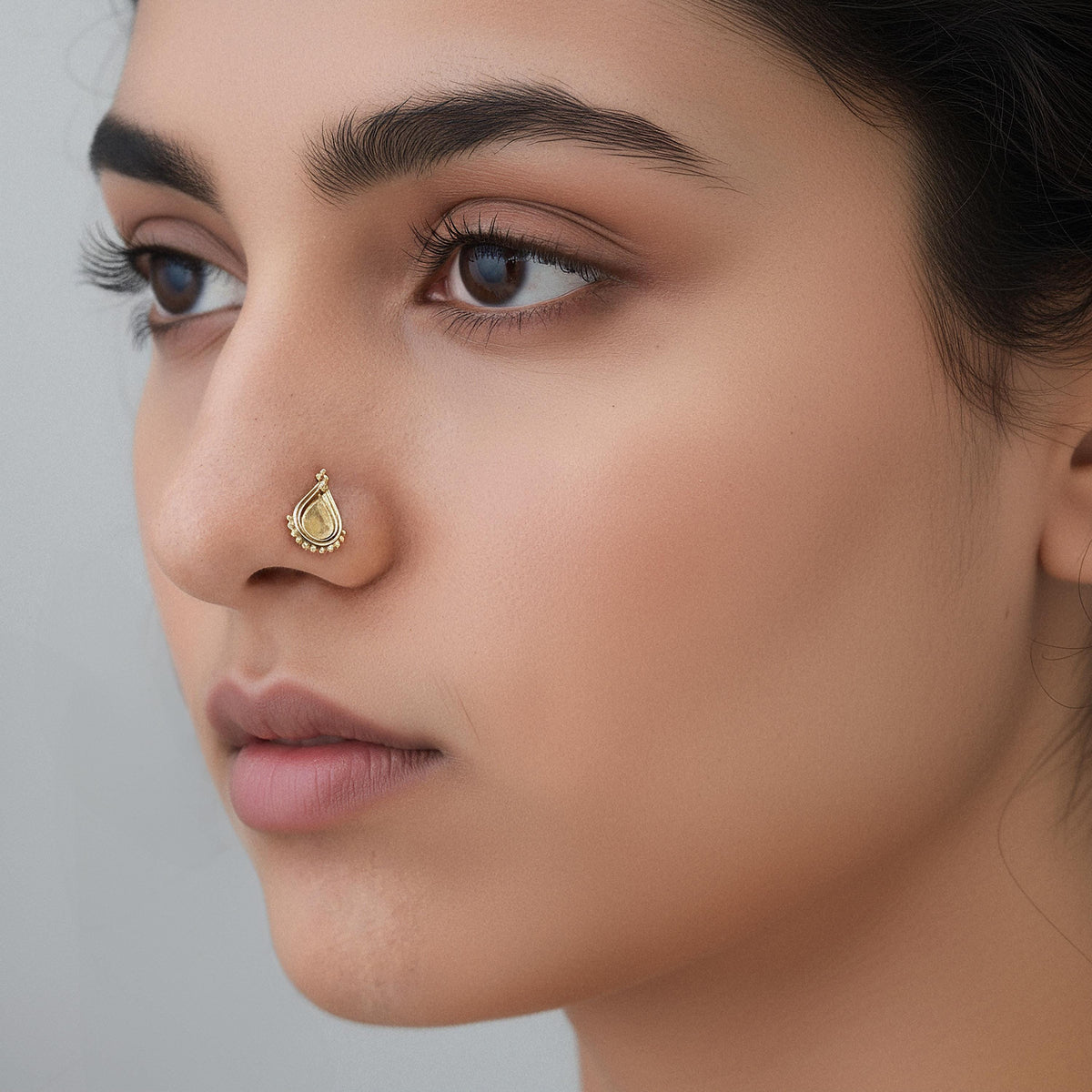 A close-up portrait of a woman with a gold nose ring, her gaze directed off to the side.