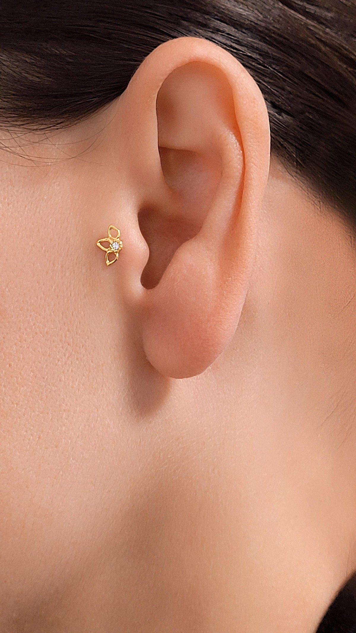 A gold-colored earring with a small flower-like design is visible in the ear.