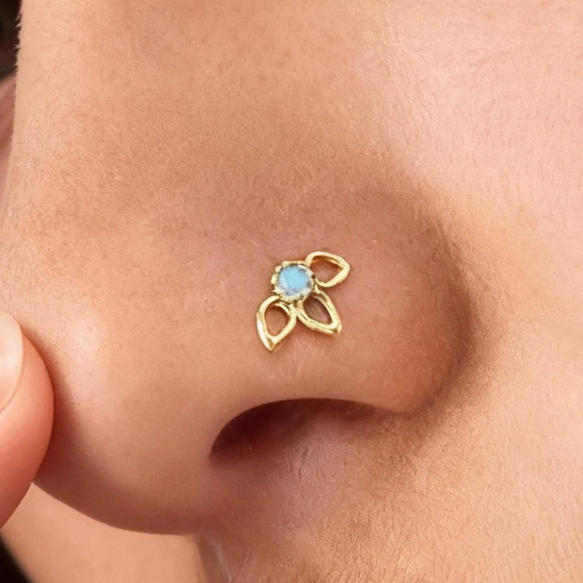 A close-up of a person's nose with a small gold nose ring featuring a blue gemstone.