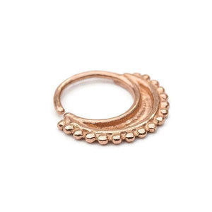 A copper-colored metal nose ring with a decorative, textured design.