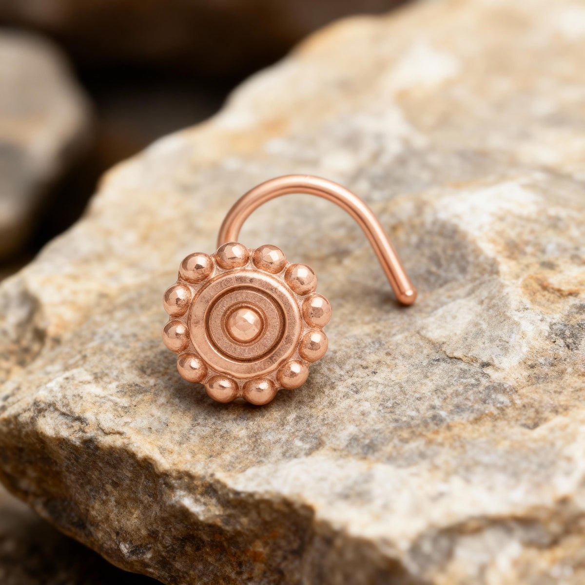 A copper-colored nose ring with a circular design sits on a rock.