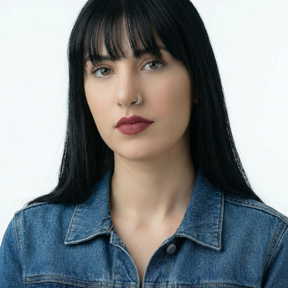 A portrait of a woman with long dark hair wearing a denim jacket, looking directly at the camera with a serious expression.
