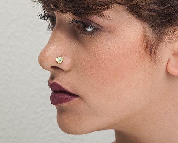 A close-up of a woman's face, focusing on her nose and lips. She has dark hair and is wearing a gold nose ring.