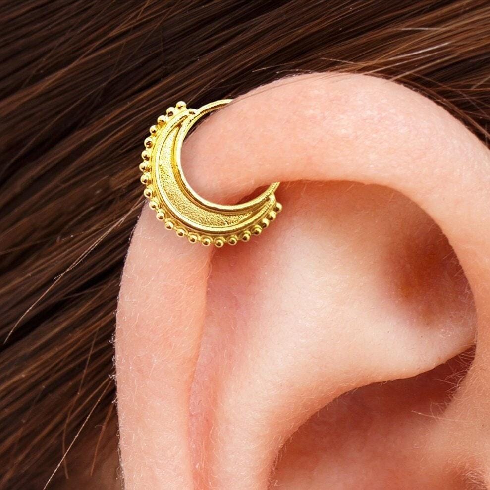 Cartilage Nose Ring: A gold earring with a crescent moon design is shown in close-up, resting on the side of an ear.