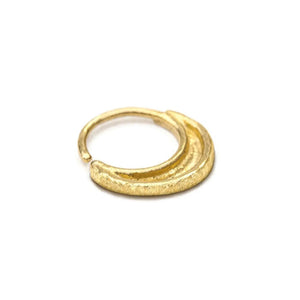 A gold-colored metal ring with a curved design, resting on a white background.