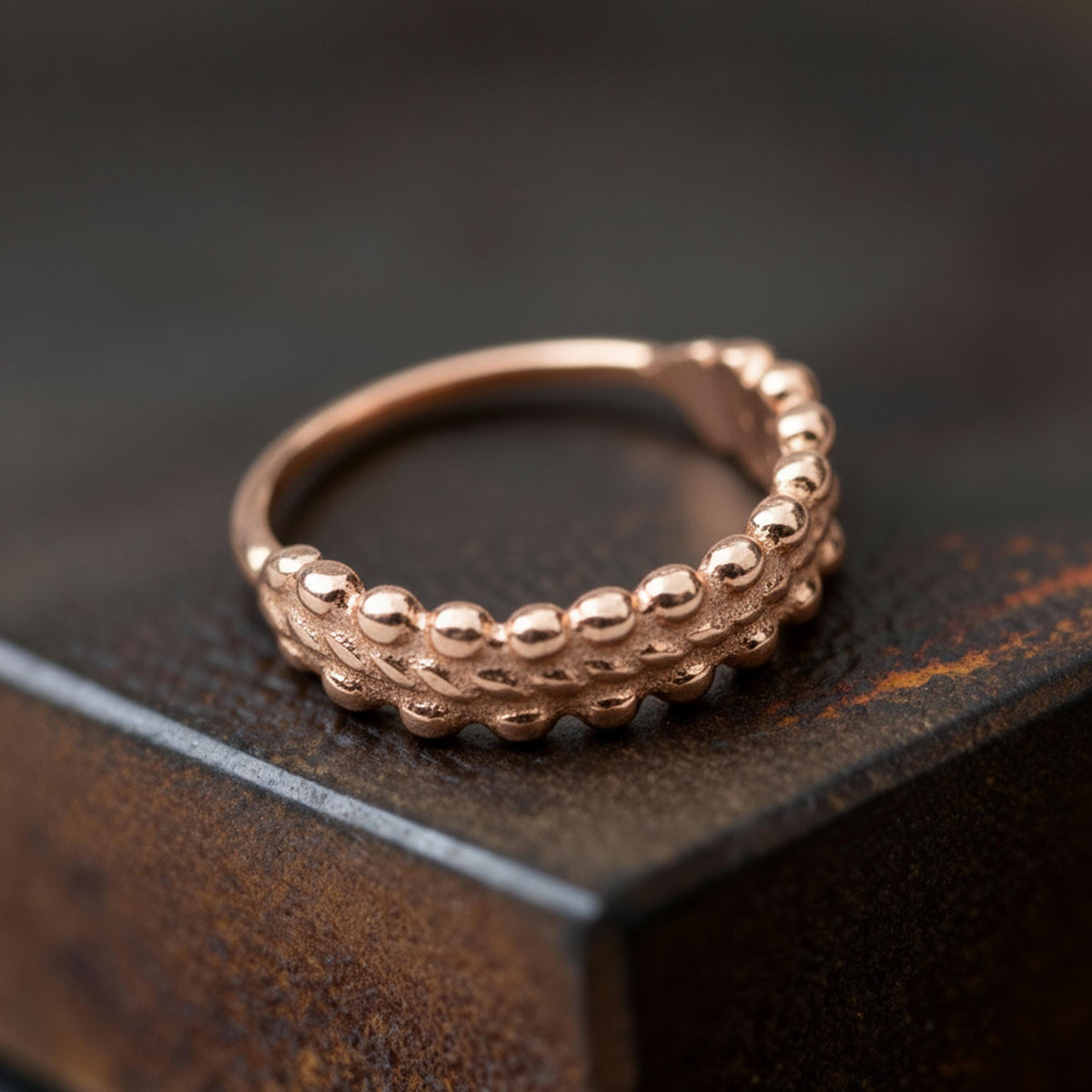 A close-up image of a gold ring with a textured band, resting on a dark surface.