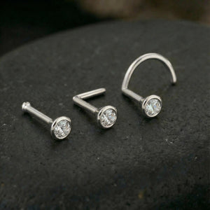 Three white gold nose piercings with diamonds are displayed on a dark surface.