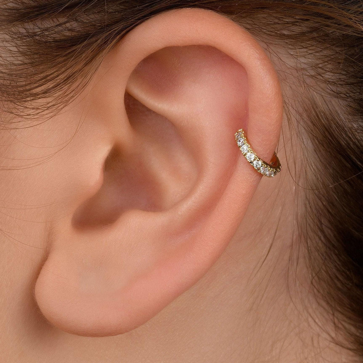 A close-up view of a person's ear with a gold-colored earring featuring small diamonds.
