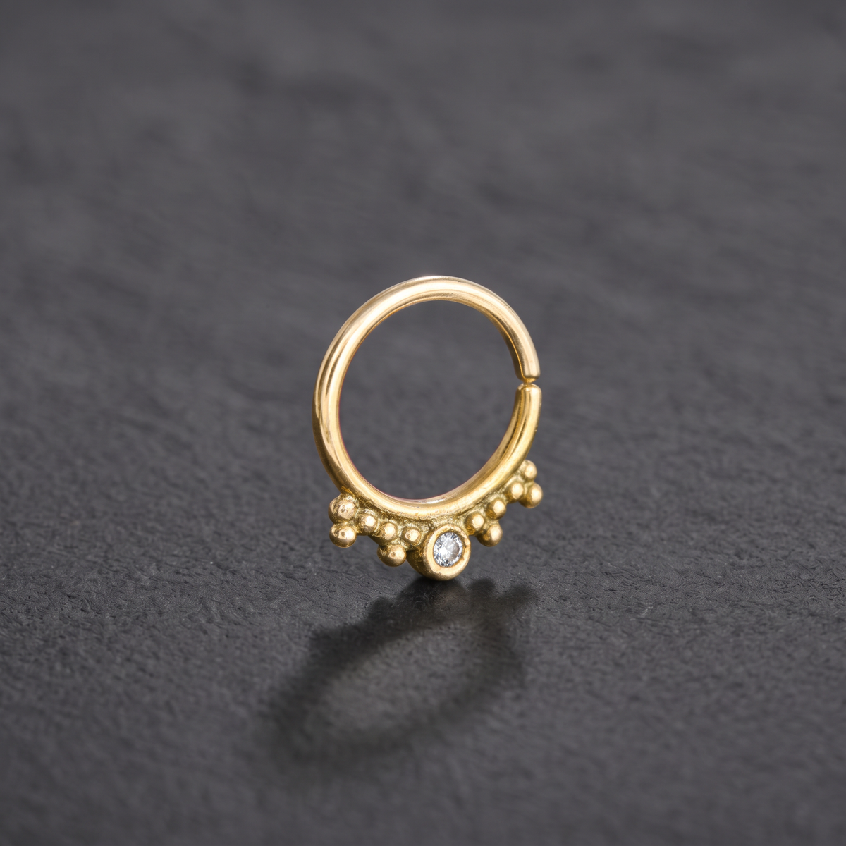 A gold-colored ring with a small diamond in the center, resting on a dark surface.