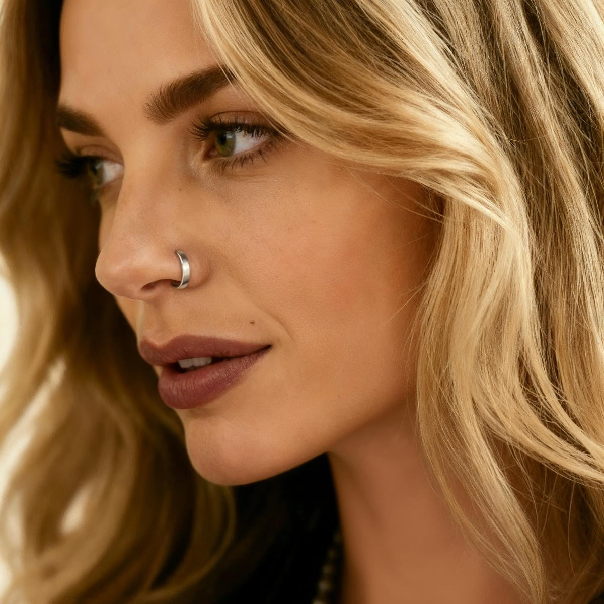 A close-up portrait of a woman with blonde hair, wearing a nose ring and looking off to the side.