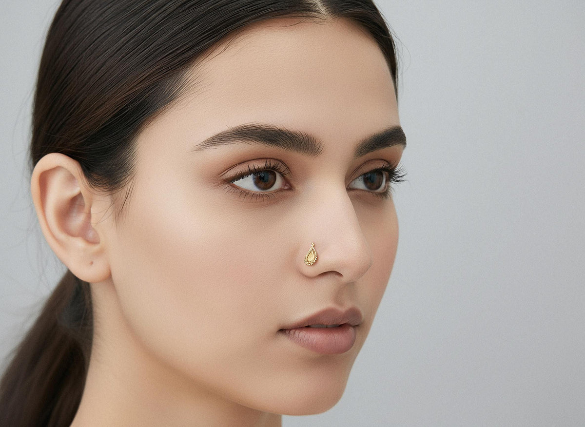 A close-up portrait of a woman with dark hair and a gold nose stud, looking off to the side with a neutral expression.