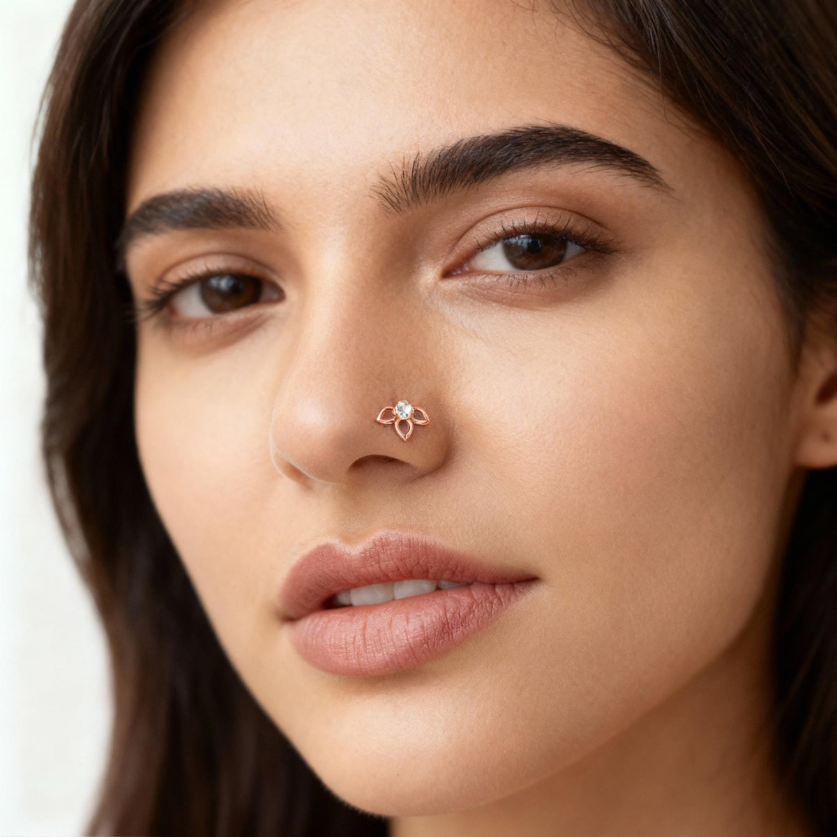 A close-up portrait of a woman with dark hair and a nose ring, looking directly at the camera with a neutral expression.