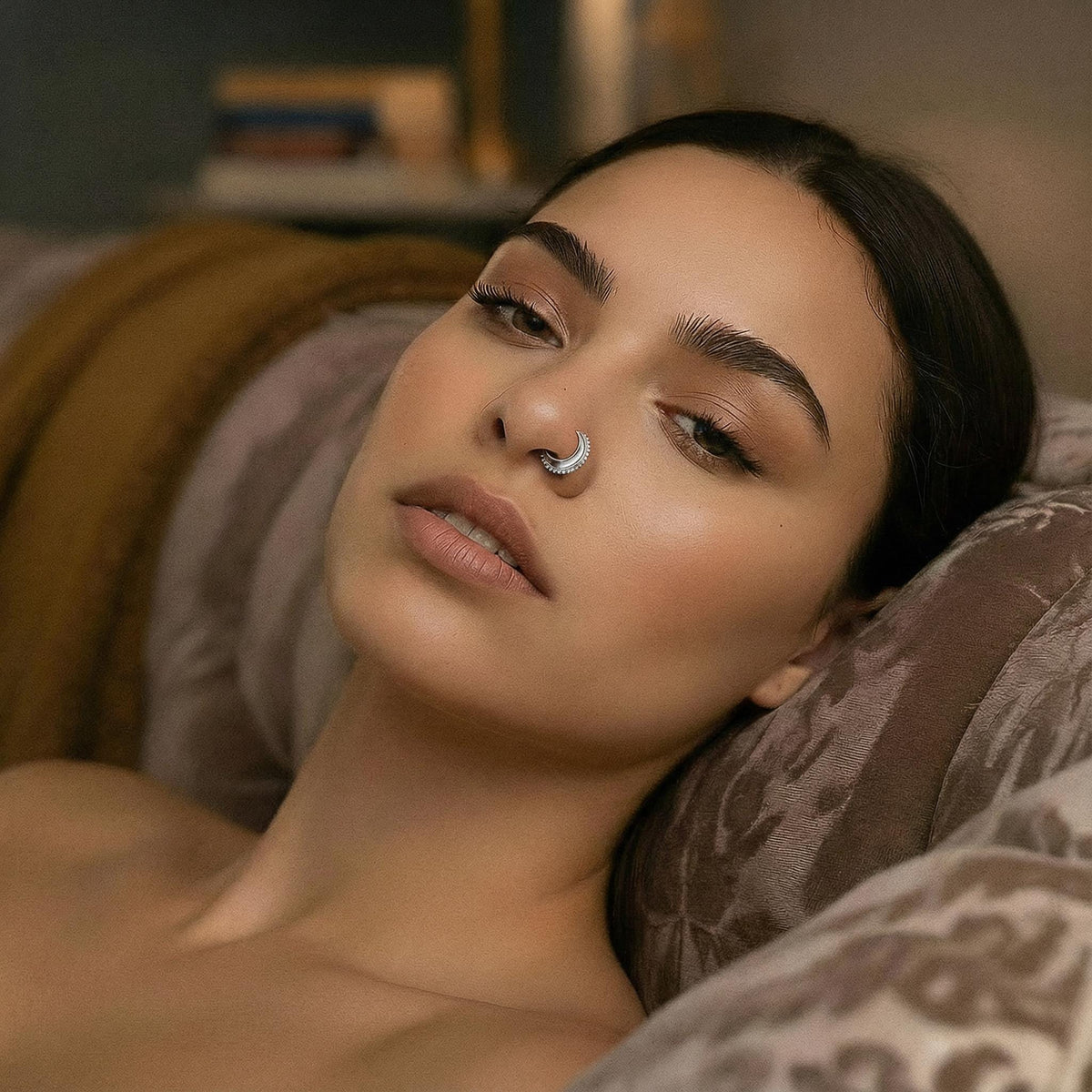 A woman with dark hair and a nose ring is lying on a patterned couch, looking pensive.