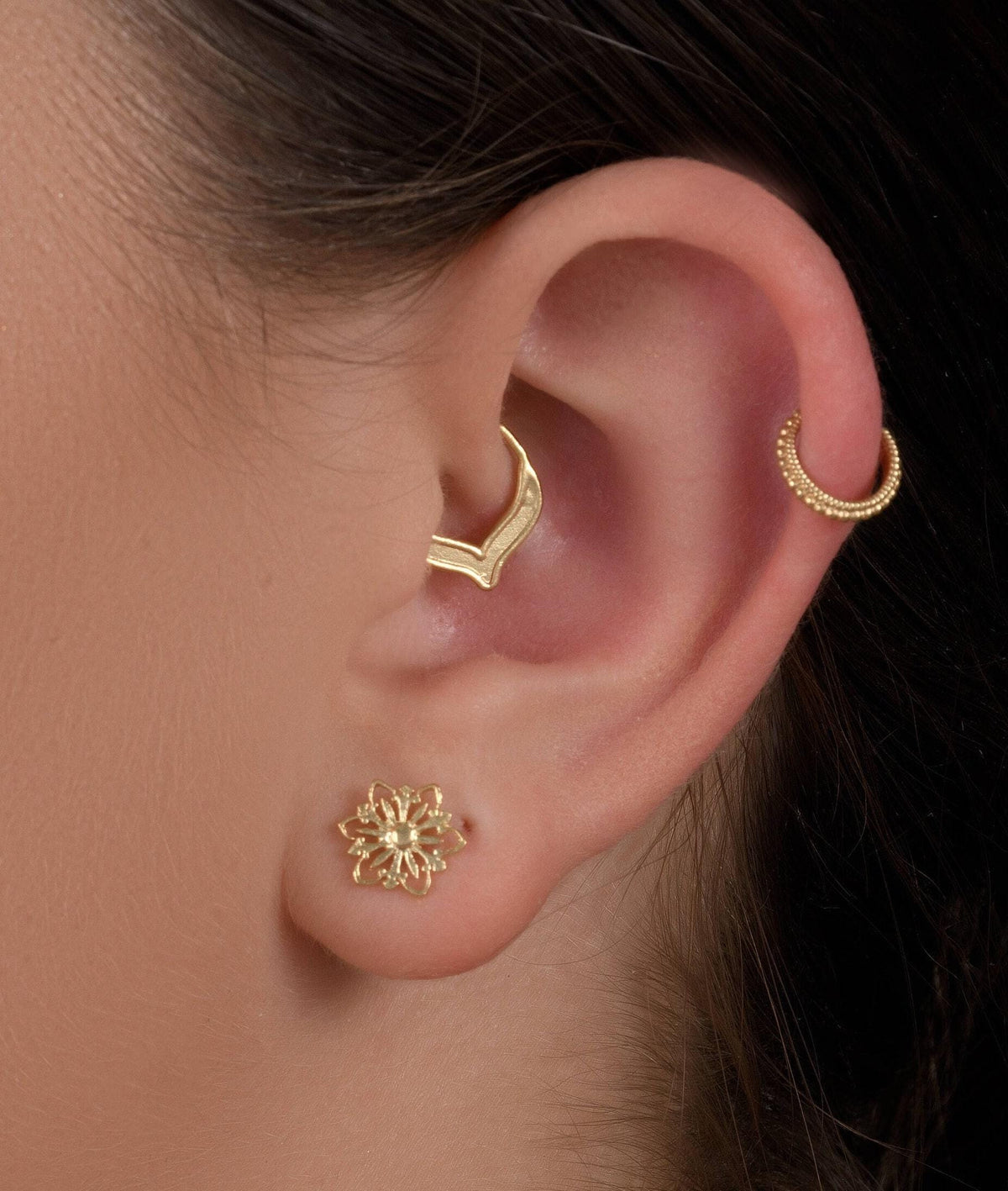 A close-up of a person's ear adorned with gold earrings and a gold ring, showcasing the intricate details of the jewelry.