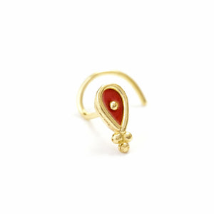 A gold-colored nose ring with a red gemstone in the center.