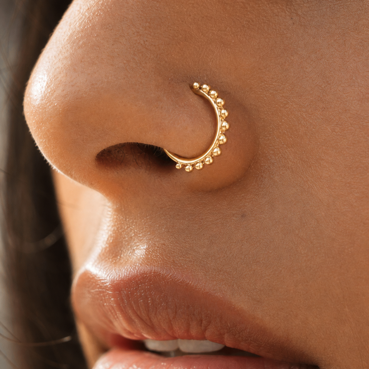 A close-up of a person's nose with a gold-colored nose ring featuring a decorative design.