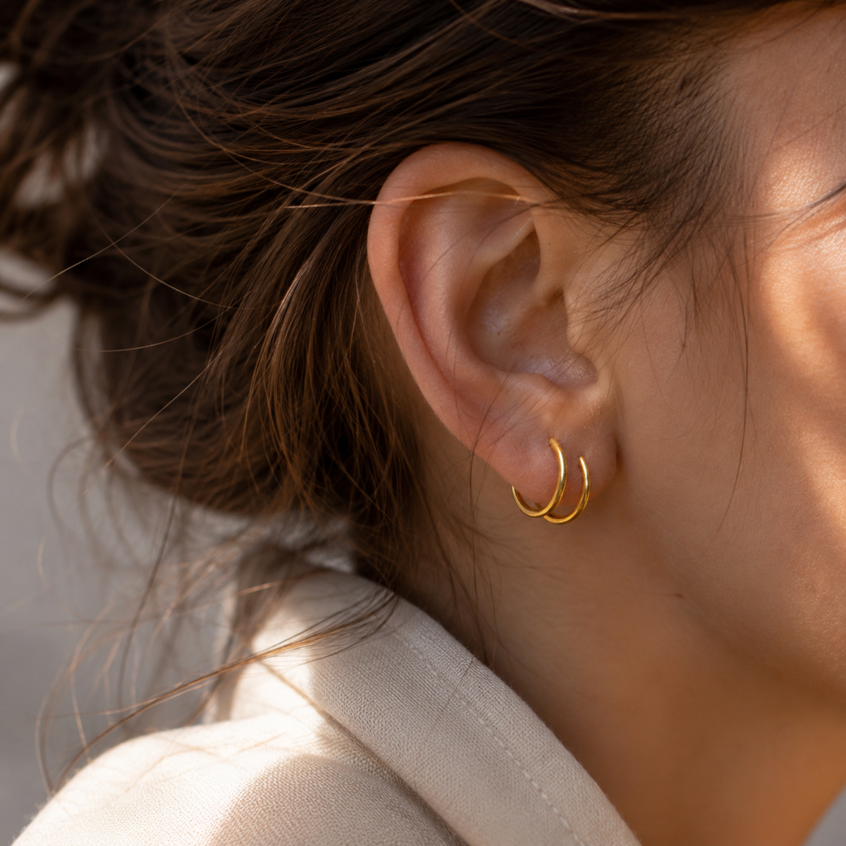 A close-up view of a person's ear adorned with a pair of gold hoop earrings.