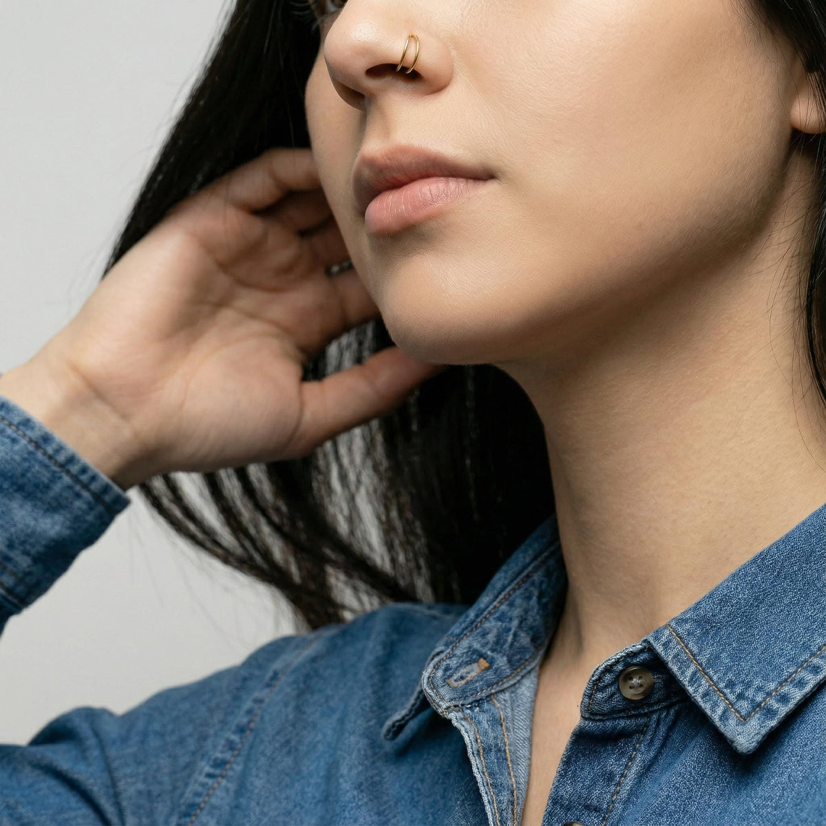 A close-up of a person's face, focusing on their hand and nose, wearing a denim shirt.