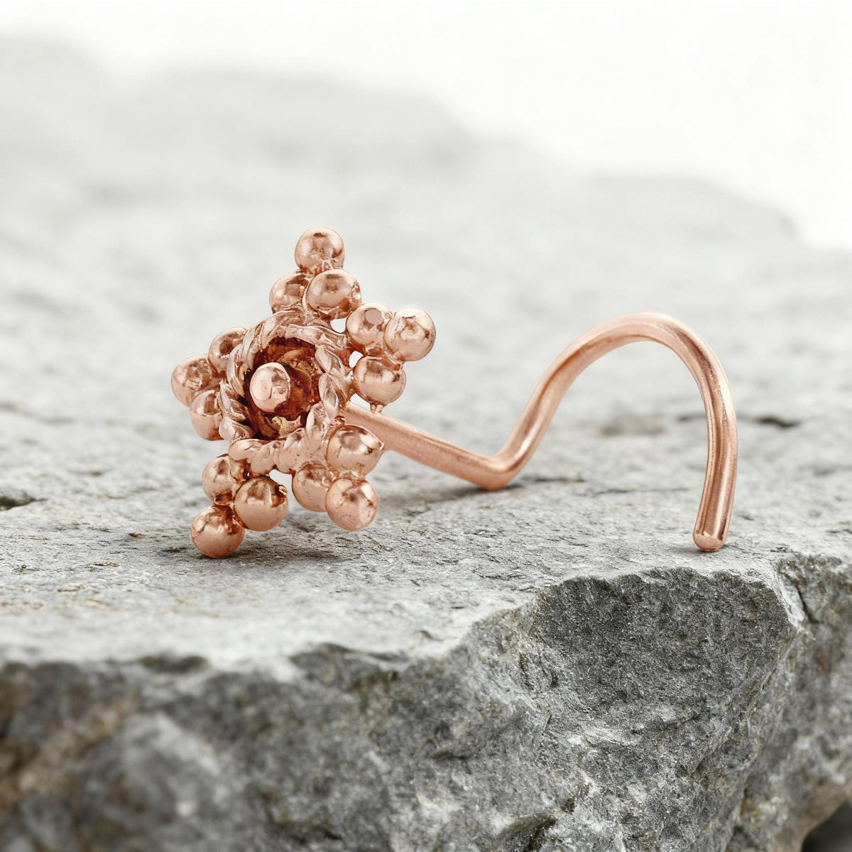 A copper-colored nose ring with a floral design rests on a gray rock surface.