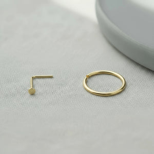 a gold-colored nose ring and a gold-colored ring on a white surface.