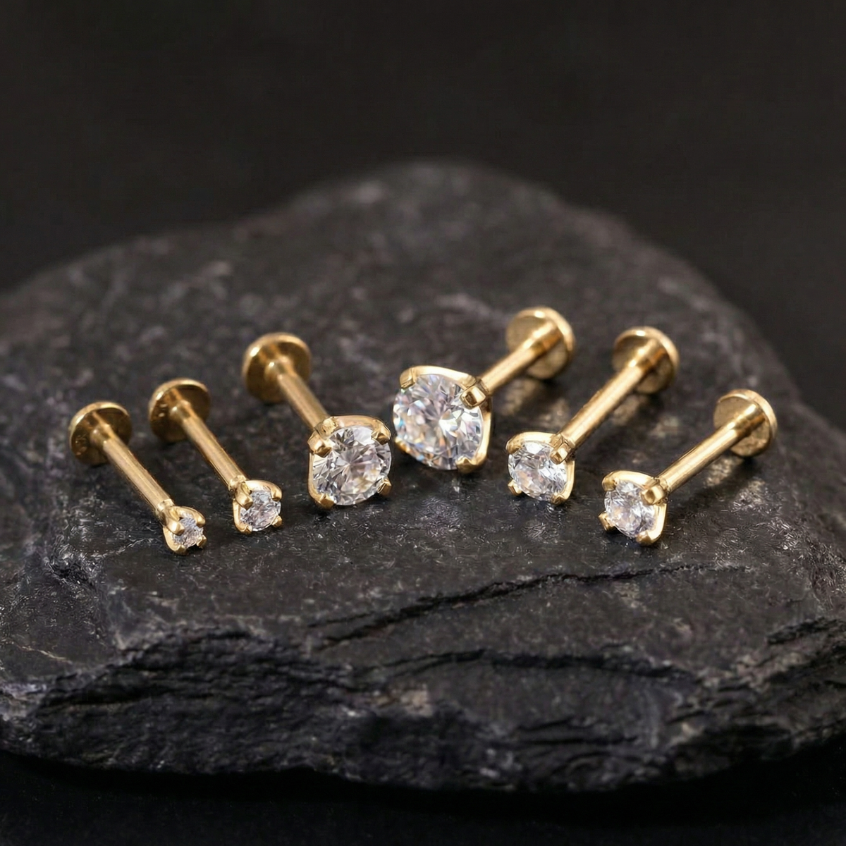 A collection of gold-colored diamond earrings is displayed on a dark surface, with the largest earrings in the center and smaller ones surrounding them.