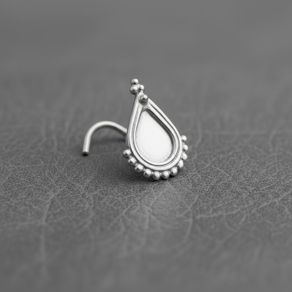 A silver nose stud with a decorative pendant is shown against a textured gray background.