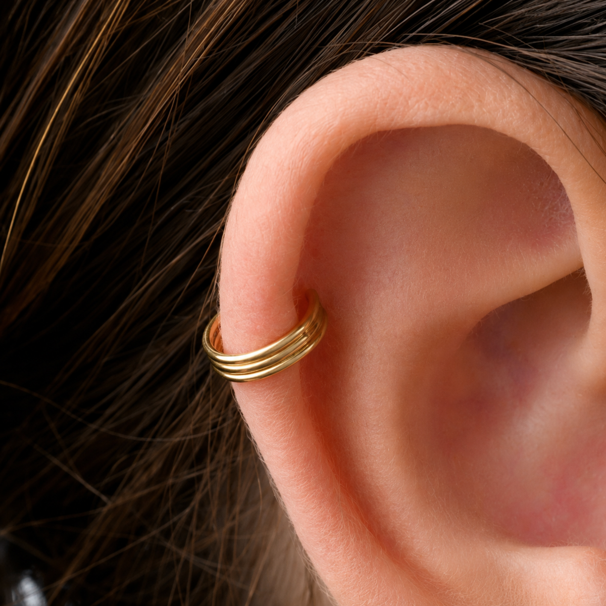 A gold ring is placed on the side of an ear.