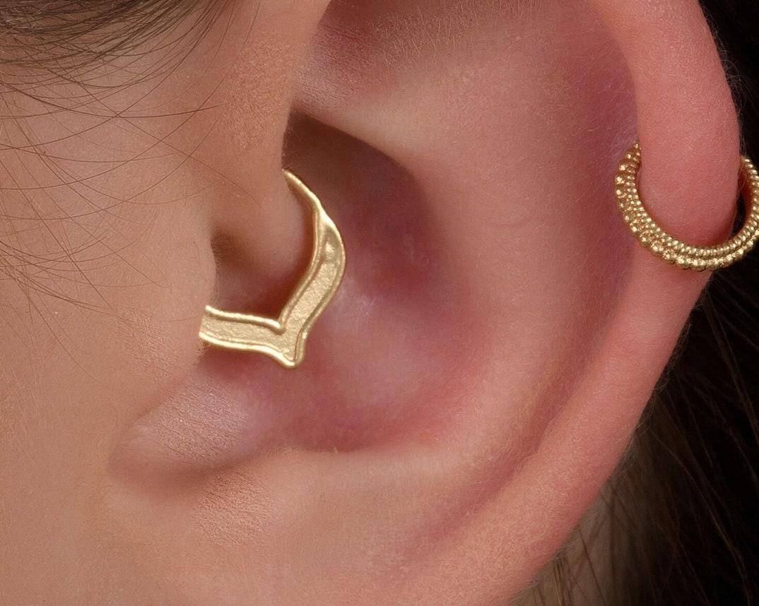 A close-up of a person's ear with a gold-colored earring in the earlobe.