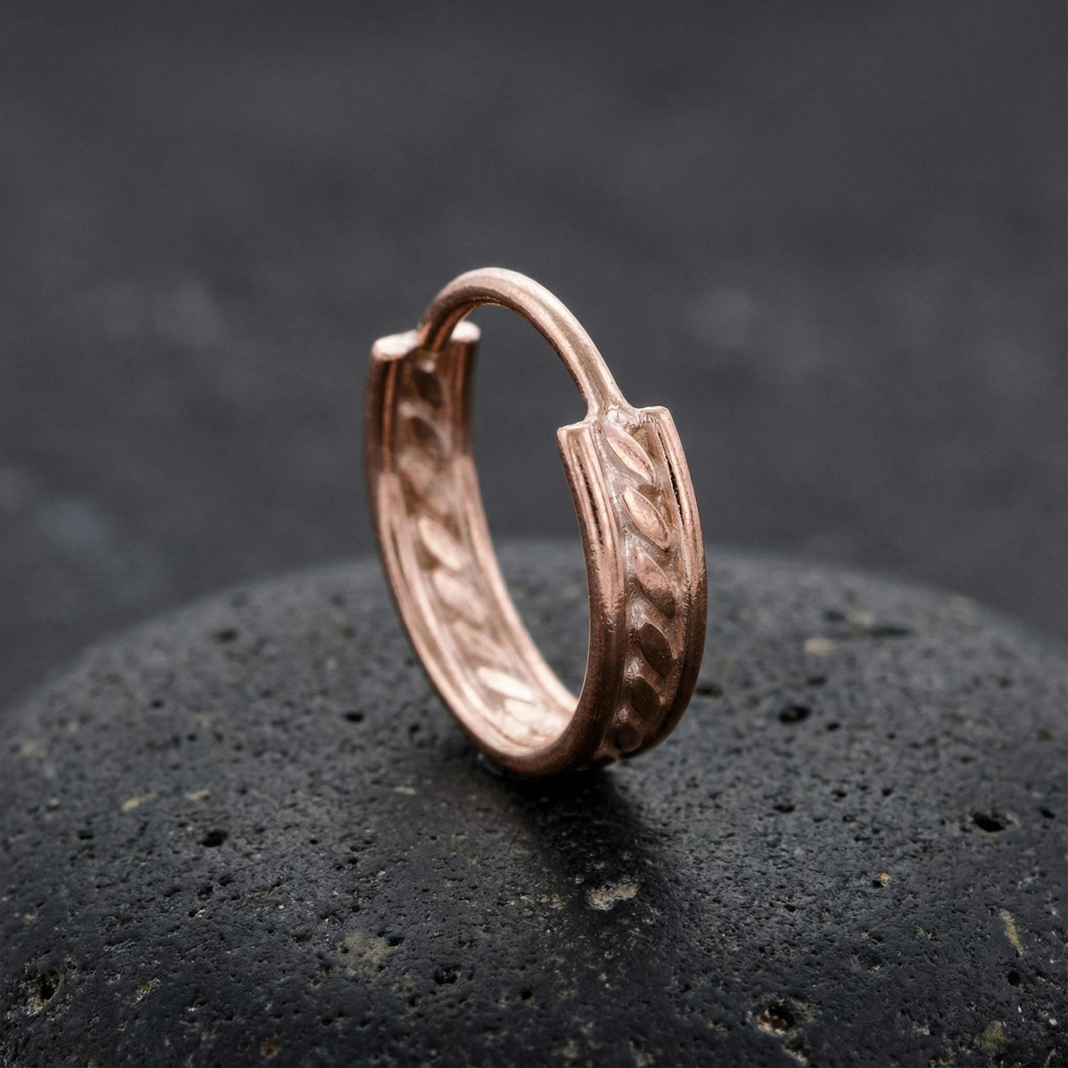 A copper-colored earring with a twisted design sits on a dark surface.