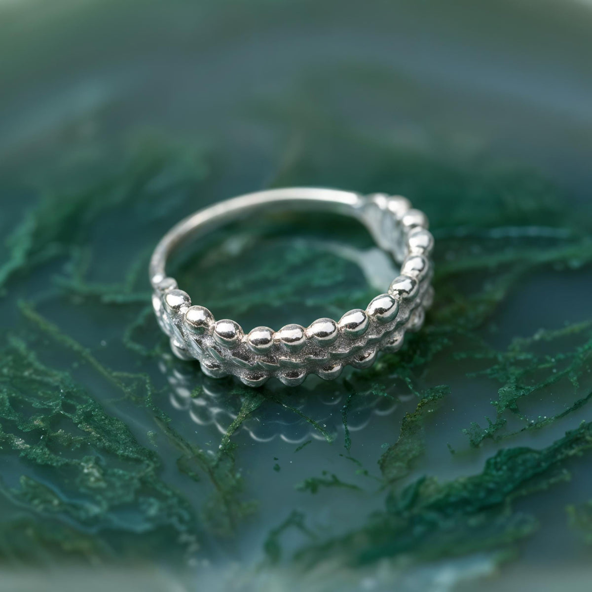 A silver ring with a unique, textured design sits on a green, mossy surface.