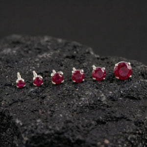 A collection of red gemstone earrings is displayed on a dark surface, with the largest earrings positioned in the center and the smaller ones arranged around them.
