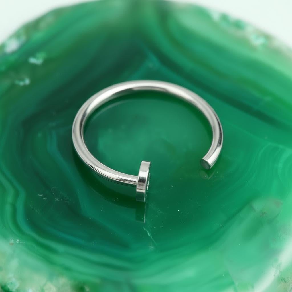 A silver ring with a curved band is resting on a green marble surface.