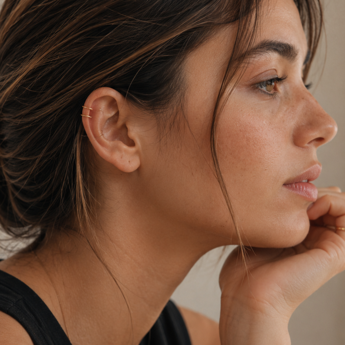 A close-up profile view of a woman with dark hair, wearing a black top and earrings.