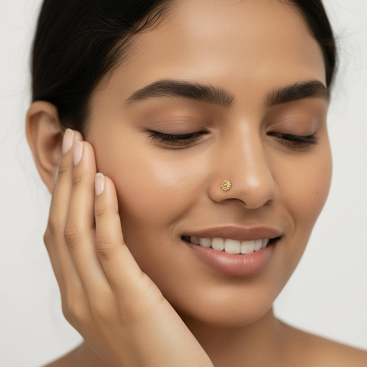 A close-up portrait of a smiling woman with her eyes closed, her hand gently touching her face.