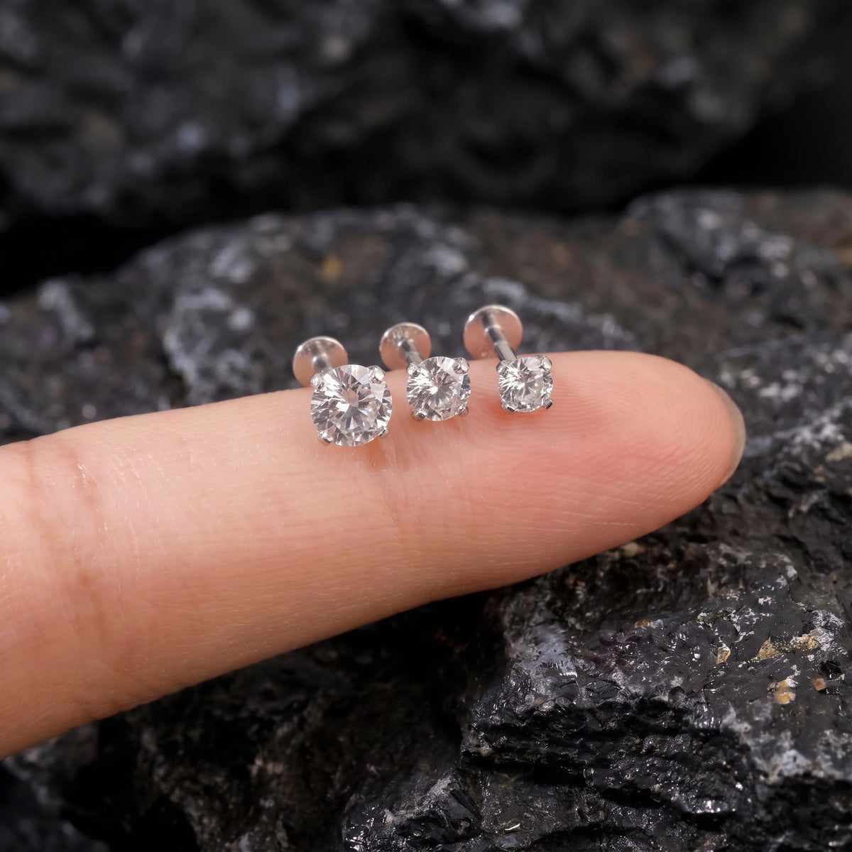 A close-up image of a person's finger wearing three small diamond earrings.