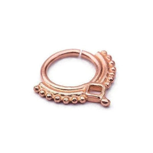 A copper-colored metal ring with a decorative design, featuring a square-shaped element and a row of small beads or dots along the edge.