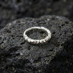 A silver ring with a unique, textured design rests on a dark, rocky surface.
