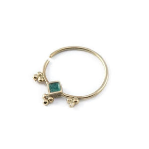 A gold-colored nose ring with a green gemstone in the center.