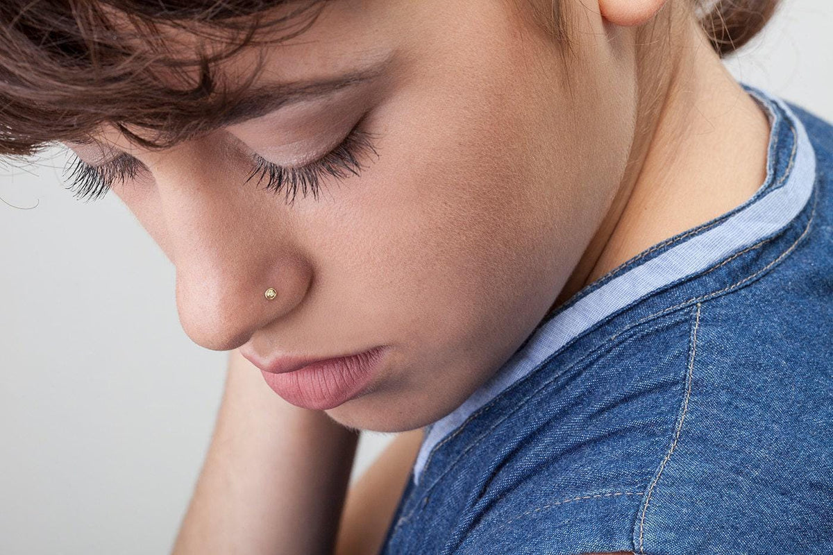 A close-up of a person's face, with their eyes closed and a nose piercing visible.