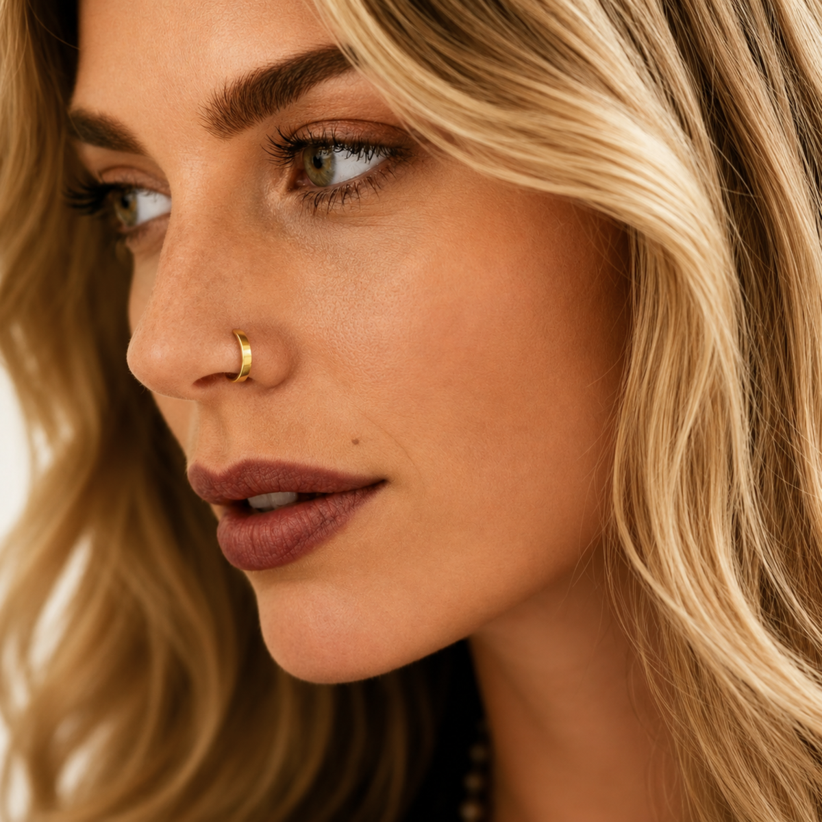 A close-up portrait of a woman with blonde hair, wearing a nose ring and looking pensive.