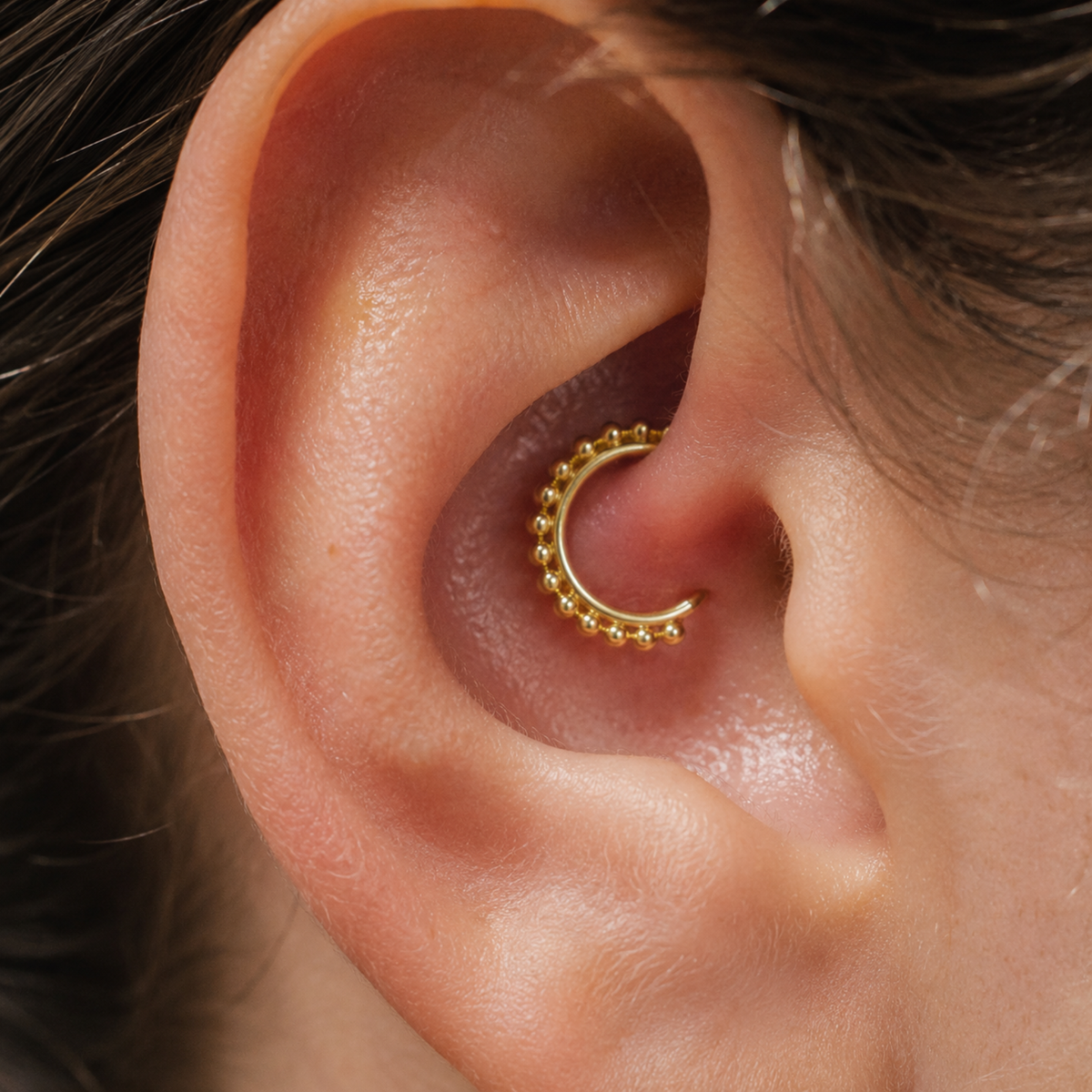 A close-up view of a person's ear with a gold-colored metal ring or earring inserted.