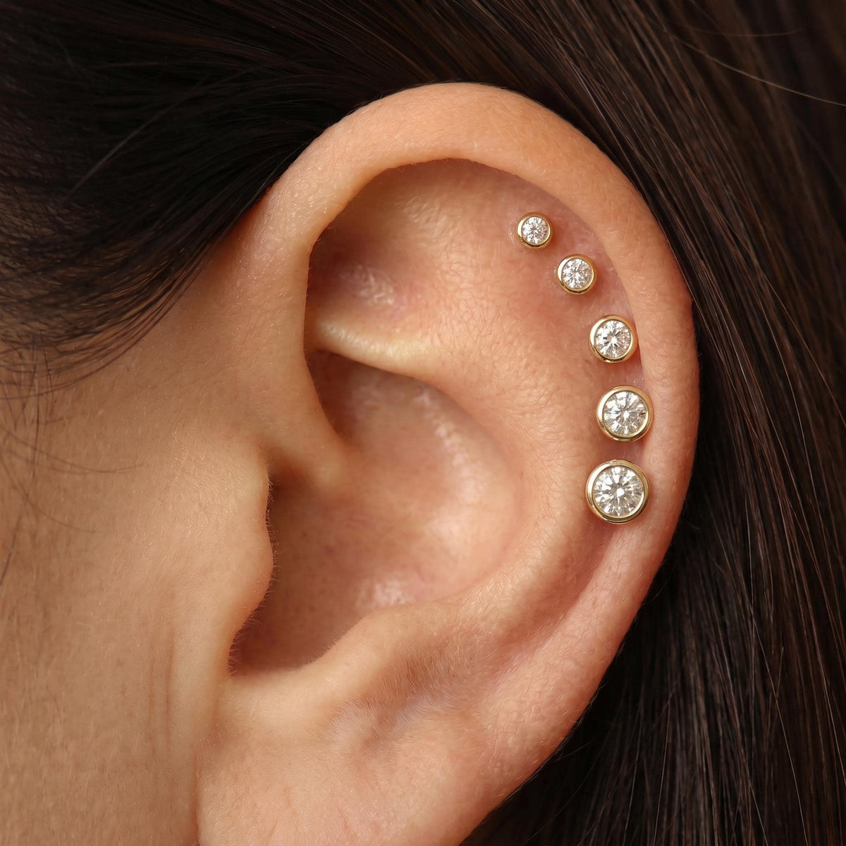 A close-up of a person's ear with several diamond-encrusted earrings.