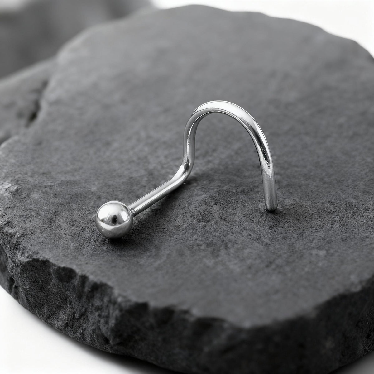 A silver piercing ring with a ball at the end rests on a gray rock.