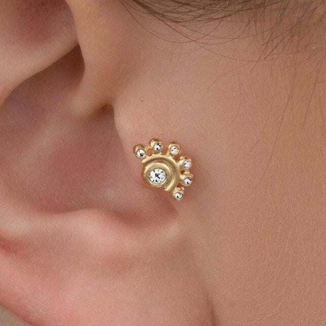 Diamond Tragus Earring: A close-up view of a person's ear with a gold earring featuring a floral design.