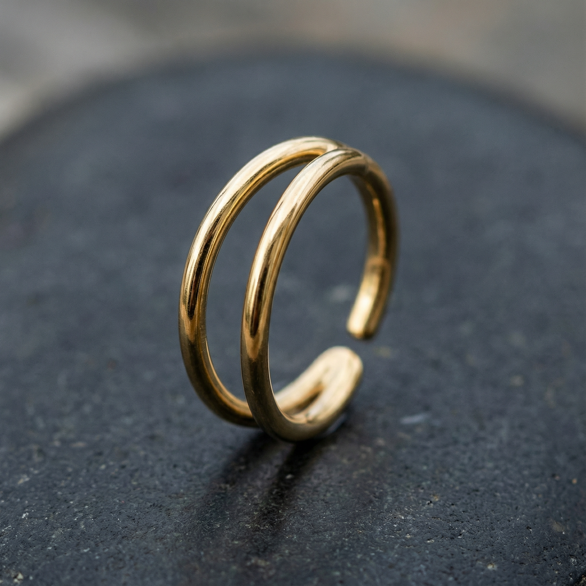 A gold ring with a twisted design sits on a dark surface.