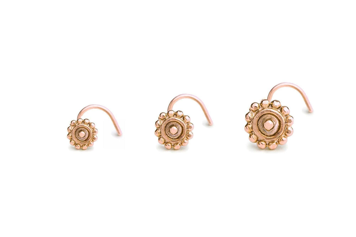 three small, ornate gold-colored nose studs arranged in a row.